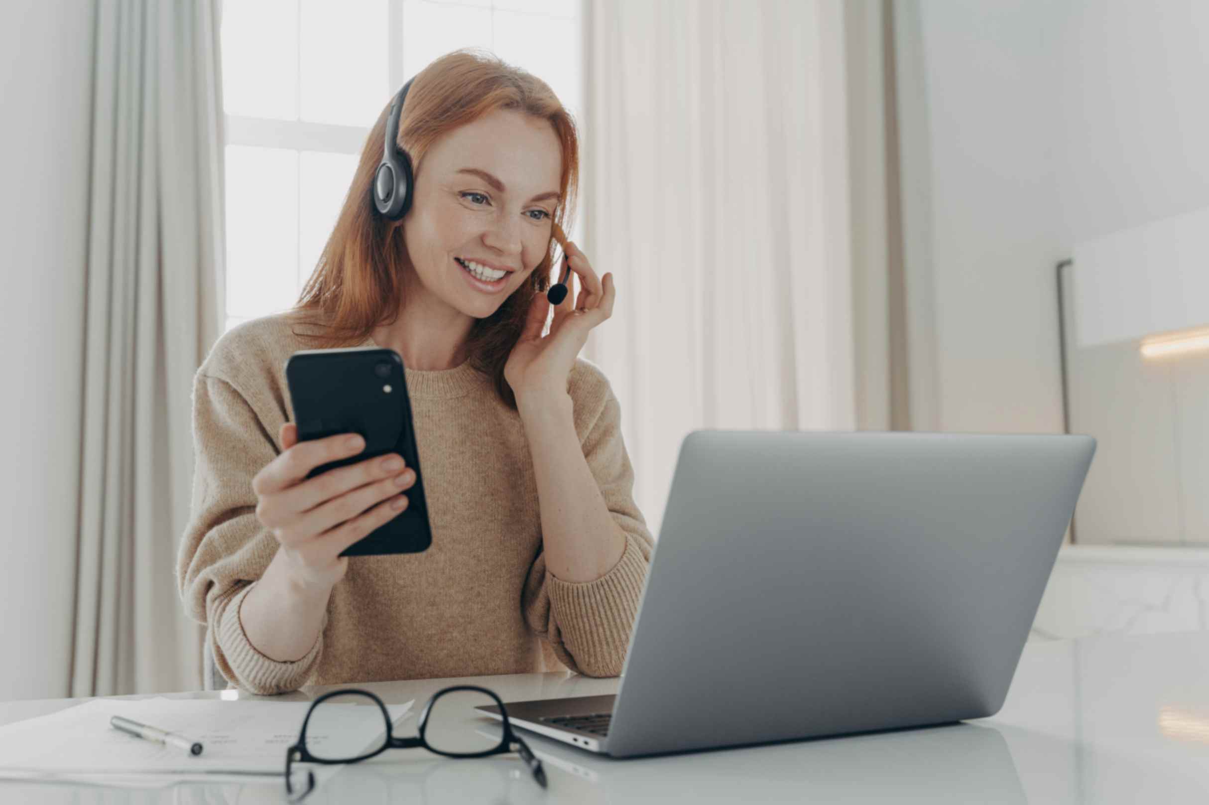 woman-smiling-using-cellphone-with-laptop-and-headphones